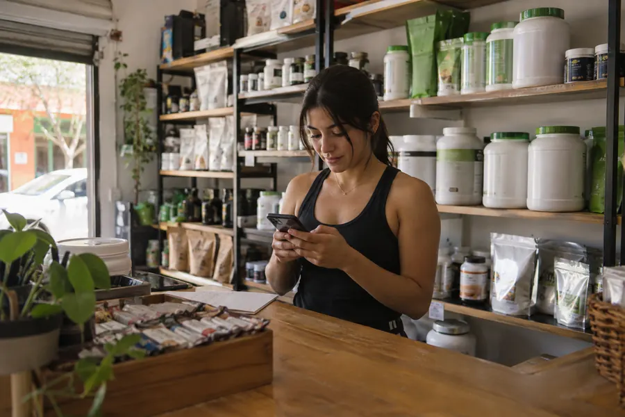 Dueña de una tienda de suplementos leyendo un mensaje en su teléfono detrás del mostrador